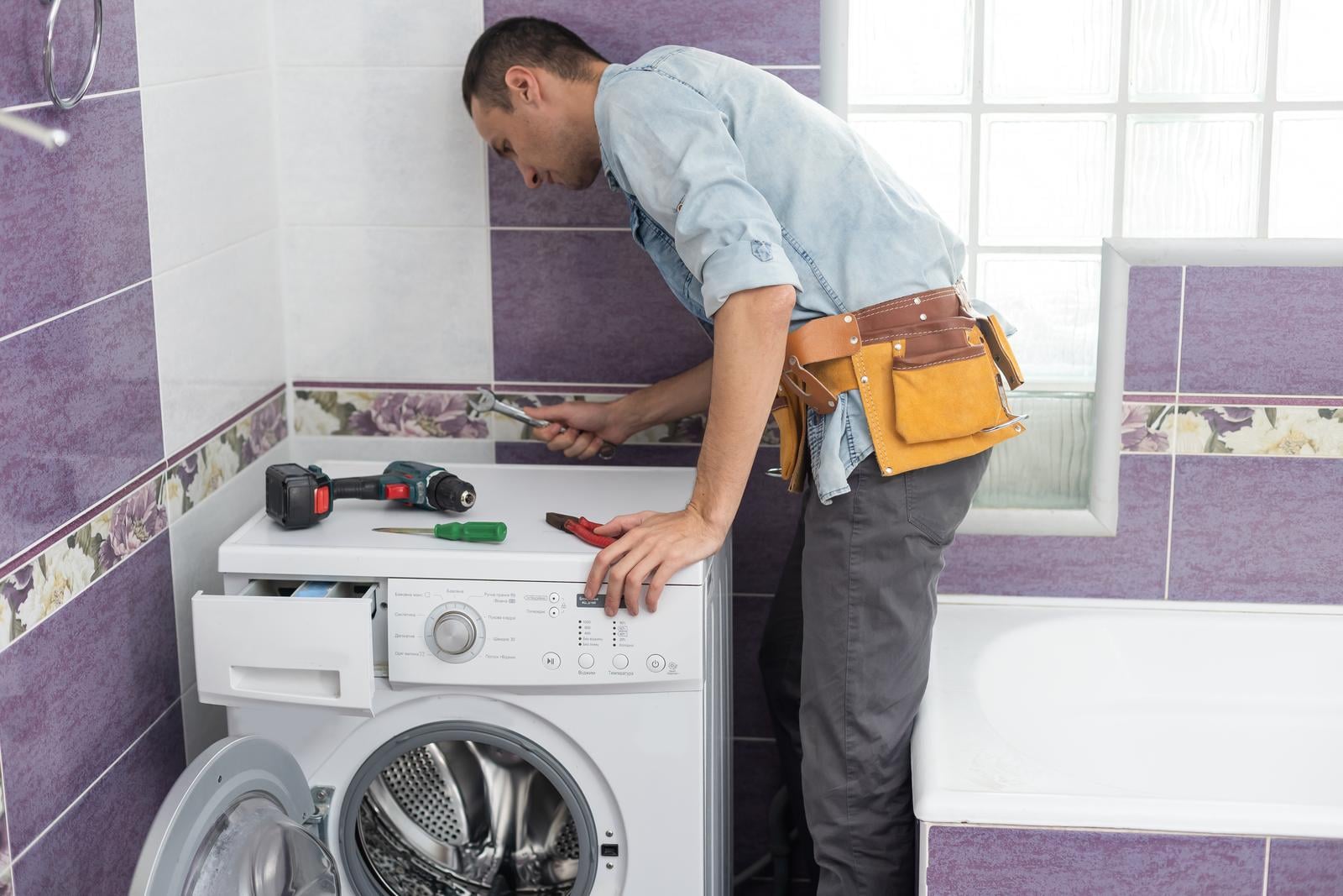 47284322 The Young Handsome Repairman In Worker Suit With The Professional Tools Box Is Fixing The Washing Machine In The Bathroom Min